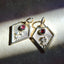 Two gold pendants with red gemstones on a textured surface