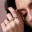 Close-up of a hand wearing multiple gold rings with gemstones on a neutral background