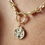 Gold necklace with a round pendant featuring a floral design and a central gemstone, worn on skin.