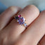 A colored gemstone cluster ring with a pink and purple color palate. Made with different hues and sizes of round colored gemstones set on a gold band.