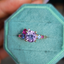 A colored gemstone cluster ring with a pink and purple color palate. Made with different hues and sizes of round colored gemstones set on a gold band.
