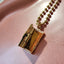 A gold book locket with a diamond on the right hand center at the opening. Finished with ray designs and jump ring bail.
