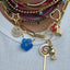 A gold lollipop charm with colored gemstone in lay. The head of the lollypop has a swirl pattern where the stone in lay is set.