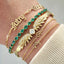 Gold and green gemstone bracelets on a wrist against a neutral background
