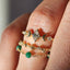 Close-up of a hand wearing three gold rings with gemstones on a blurred background