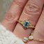Close-up of a hand wearing a gold ring with a blue gemstone and matching earring.