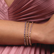Model wearing a 14K yellow gold bracelet with garnet, amethyst, and pink tourmaline stones on a pink dress.