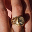 Gold ring with diamond on a finger against a pink background