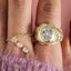 Gold ring with diamond on a finger against a pink background