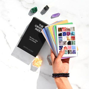 Hand holding a card with crystal images next to 'The Crystal Index' book on a white marble surface.