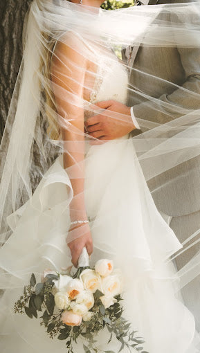 Close-up of a bride and groom with the bride holding a bouquet, surrounded by a veil.