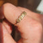 Gold ring with leaf design on a finger against a blurred background