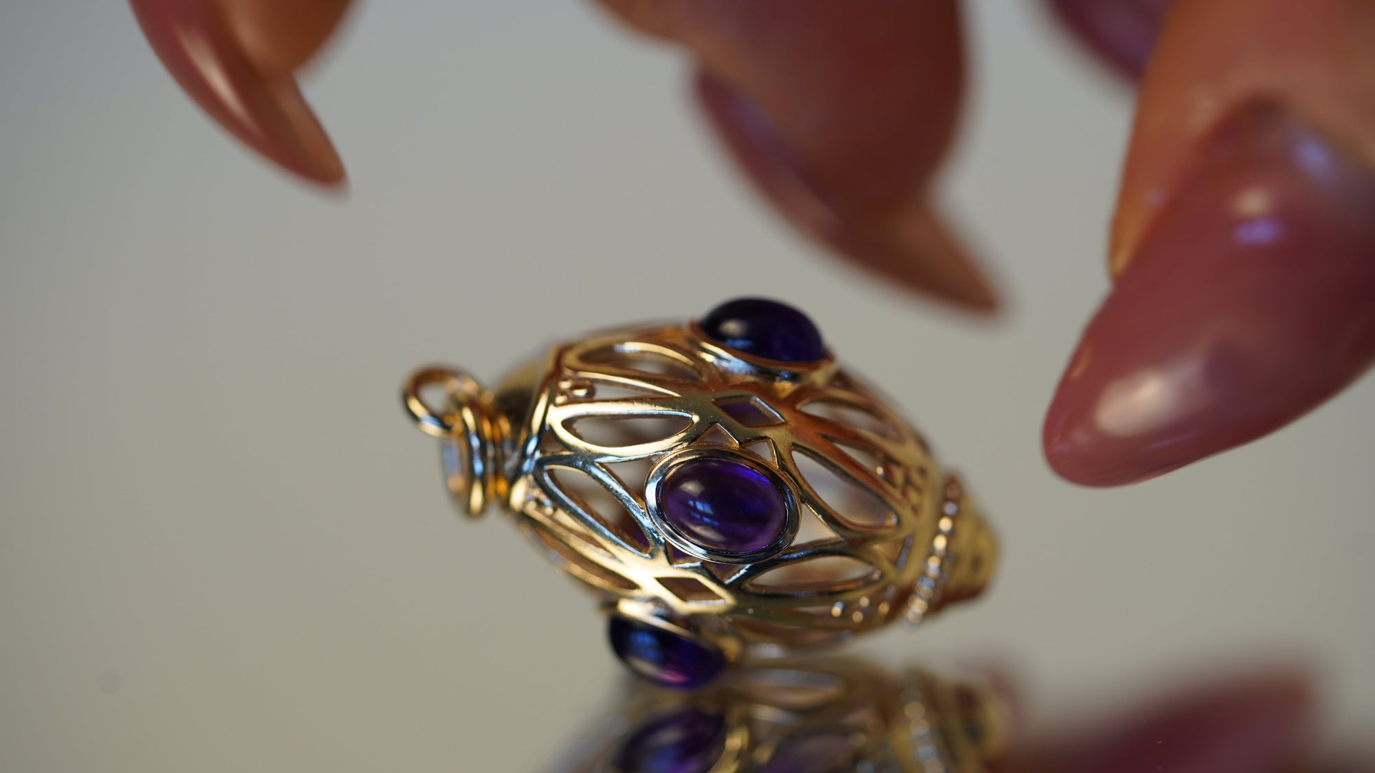 Gold pendant with purple gemstones held by a hand on a reflective surface