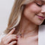 Woman wearing a gold necklace with a diamond pendant against a neutral background