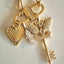 Gold necklace with heart, key, and shell charms on a light background