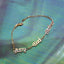 Gold bracelet with letter charms on a textured green fabric background