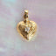Gold heart-shaped pendant with a diamond on a textured pink and purple background