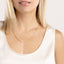 Close-up of a person wearing a gold necklace on a plain background