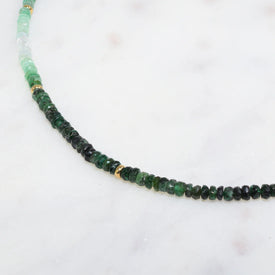 A emerald necklace with an ombre look, created with different shaded green and gold bead spacing. 