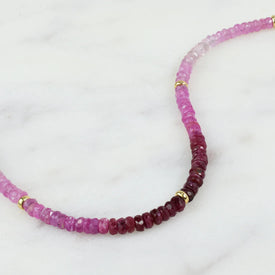 A ruby necklace with an ombre look, created with different shaded green and gold bead spacing. 
