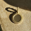 A gold coin disc with a polished surface for optional engraving. Finished with gold beaded design on the outer frame and bail. 