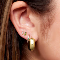 Close-up of a model wearing gold earrings with emerald and diamond accents.