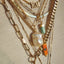 A necklace stack with the free form pearl necklace stacked with other gold chains and orange evil eye charm.