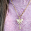 Gold necklace with a leaf pendant on a pink textured background