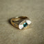 A elongated oval signate ring with a round emerald set on the center of the face. With two eight pointed starts on both sides of the shank. 