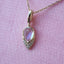 Gold necklace with a teardrop-shaped pink gemstone pendant on a pink background
