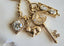 Gold necklace with various charms including a key, rabbit, and heart on a white background.