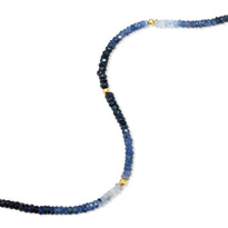 A faceted gemstone ombre beaded bracelet with three gold accents and a round clasp. 