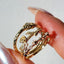 Gold ring with intricate design held between fingers against a neutral background