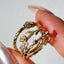 Gold ring with intricate design held between fingers against a neutral background