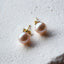 Pearl earrings with gold posts on a textured white surface