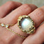 Gold necklace with a large pearl pendant held in a hand.