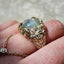 Gold necklace with a large gemstone held between fingers against a textured background