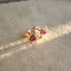 Product picture showing a pair of rose gold rose stud earrings with a ruby center on both. The pedals are in 14k rose gold along with the prongs and post and backing. Side view.