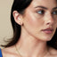 Woman wearing a gold necklace with a blue pendant and 14K yellow earrings.