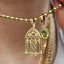 Gold necklace with a birdcage pendant and green gemstone, held by a hand.