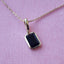 Gold necklace with a rectangular black gemstone pendant on a pink background