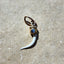 A product picture of a real rattle snake fang set with a cat eye gemstone capped top made of solid gold. The cat eye is blue with iridescent flash. 