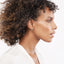 A pair of gold emerald pave huggie earrings on a model