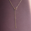 A delicate gold Y-necklace with a short drop chain and three circular ring charms, displayed on a textured dark plum background.