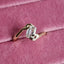 A gold ring with a clear rectangular-cut gemstone resting on a pink velvet ring box.