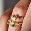 Close-up of a hand wearing three gold rings with gemstones on a blurred background