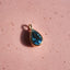 Teardrop-shaped blue gemstone pendant on a pink surface