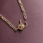 A gold paperclip chain necklace with a small elephant-shaped pendant featuring a red heart and white crystal details, displayed on a textured dark purple background.