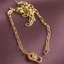 A gold paperclip chain necklace with a padlock pendant featuring a small red heart, displayed on a textured mauve fabric background.