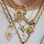 Close-up of a person wearing multiple gold necklaces with various charms on a white background